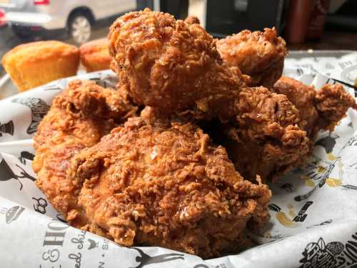 A close-up of crispy fried chicken pieces on a tray, with cornbread muffins in the background.