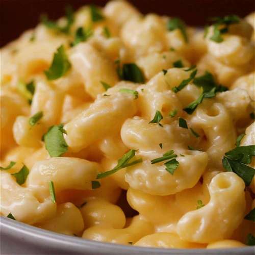Creamy macaroni and cheese topped with fresh chopped parsley in a white bowl.