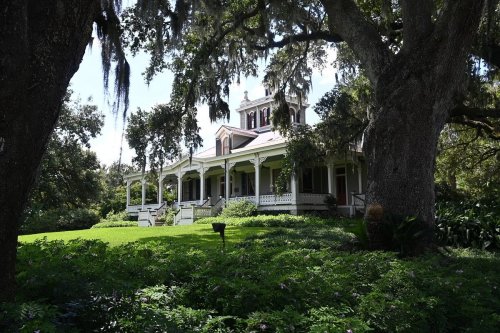 A historic house with a large porch, surrounded by lush greenery and trees draped in Spanish moss.