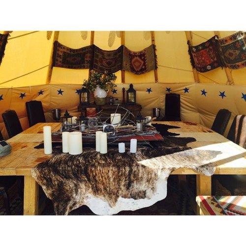 A cozy interior of a tent with a wooden table, candles, and decorative textiles, creating a warm atmosphere.