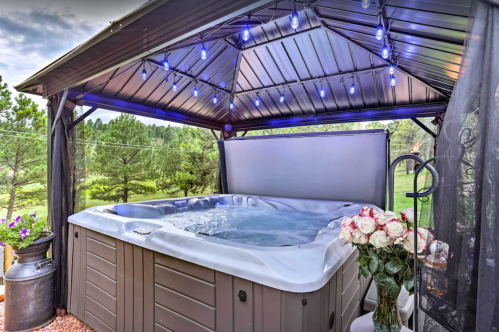 A hot tub under a gazebo with blue lights, surrounded by greenery and a bouquet of roses nearby.