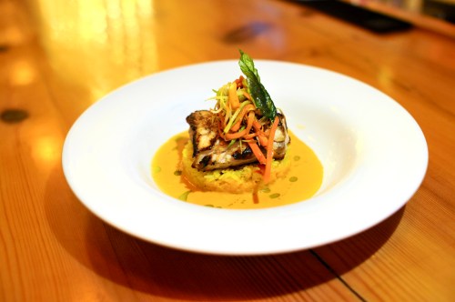 A beautifully plated dish featuring grilled fish atop a bed of rice, garnished with colorful vegetables and herbs.