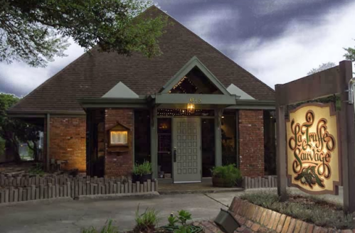 A cozy restaurant with a triangular roof, brick exterior, and a welcoming sign, set against a twilight sky.