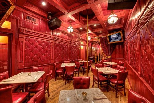 Cozy restaurant interior with red walls, marble tables, and plush seating, featuring warm lighting and elegant decor.