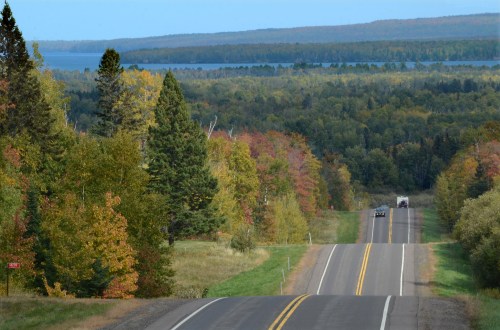 A scenic view of a winding road through colorful autumn trees, leading to a lake in the distance.