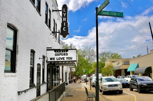 A street view of the Lyric Theater in Oxford, with a marquee reading "We Love You" and cars parked along the road.