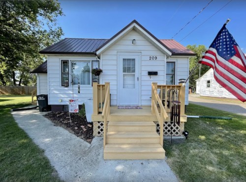 A small white house with a wooden front porch, an American flag, and a well-maintained lawn.