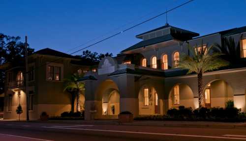 A beautifully lit building at dusk, featuring arched entrances and palm trees along the sidewalk.