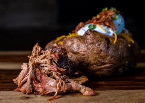 A close-up of pulled pork beside a loaded baked potato topped with cheese, sour cream, and green onions.