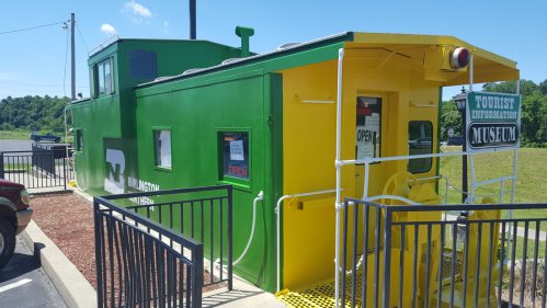 A colorful green and yellow train caboose serving as a tourist information museum, with a sign indicating it's open.