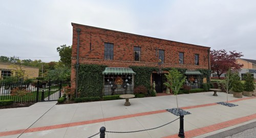 A brick building with green ivy, large windows, and a landscaped front area, featuring a stone fountain and planters.