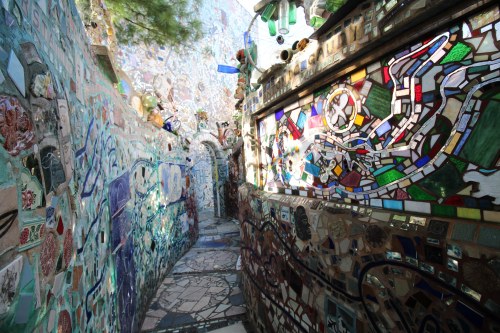 A colorful, mosaic-covered pathway with intricate designs and vibrant glass pieces lining the walls.