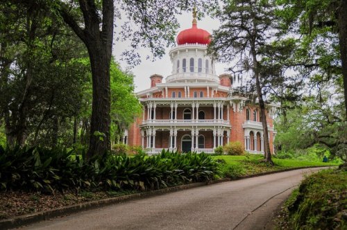 A grand, historic mansion with a red dome, surrounded by lush greenery and a winding path leading to its entrance.