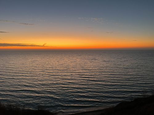 A serene sunset over calm ocean waters, with vibrant orange and blue hues reflecting on the surface.