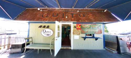 Exterior of Quito's restaurant with an open door, blue awning, and signage displaying the restaurant's name and schedule.