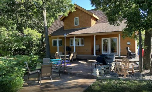 A cozy wooden house surrounded by trees, featuring a patio with outdoor seating and a fire pit.