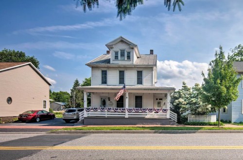A two-story white house with a porch, American flag, and bunting, set against a clear blue sky.