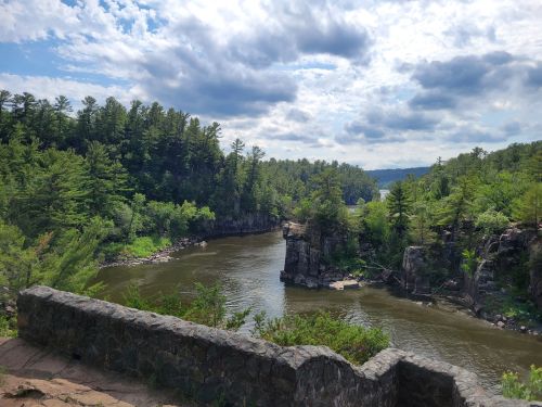 A scenic view of a river winding through lush green trees and rocky cliffs under a partly cloudy sky.