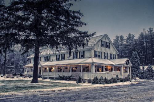 A large, charming house surrounded by snow-covered trees, illuminated warmly in a winter setting.