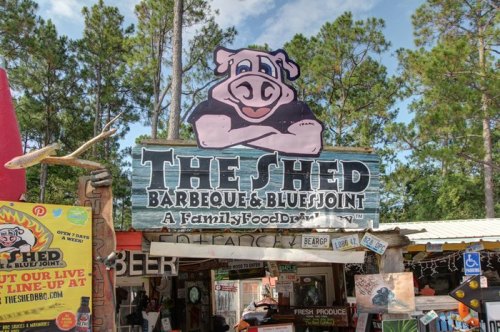 Sign for "The Shed Barbeque & Blue Joint" featuring a cartoon pig, surrounded by colorful decorations and signage.