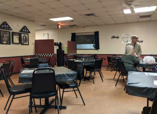 A casual dining area with empty tables, a couple conversing, and military-themed decor on the walls.