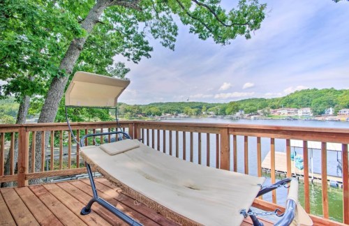 A hammock on a wooden deck overlooking a serene lake surrounded by green trees and hills.