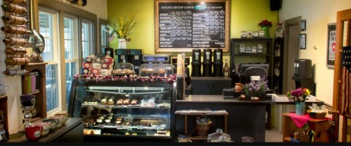 Cozy café interior featuring a display case of pastries, a menu board, and a coffee station with colorful decor.