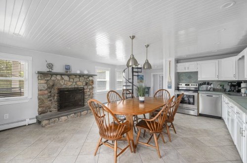 Bright kitchen with a round wooden table, six chairs, a stone fireplace, and modern appliances.