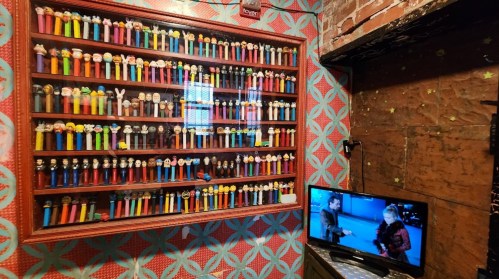 A colorful display of various Pez dispensers on a wall, with a small TV showing a scene from a movie nearby.