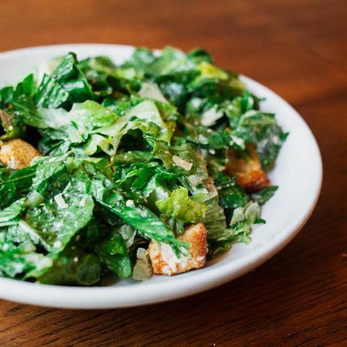 A fresh green salad with romaine lettuce, croutons, and a light dressing, served in a white bowl on a wooden table.