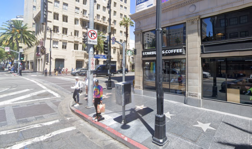 A street corner featuring a Starbucks, palm trees, and pedestrians near a traffic signal in an urban setting.