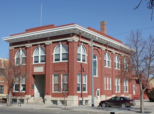 Historic red brick building with large arched windows, a flagpole, and a staircase, set against a clear blue sky.