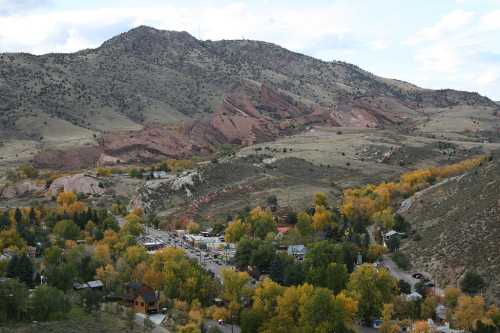 A scenic view of rolling hills with red rock formations and autumn-colored trees in a valley below.