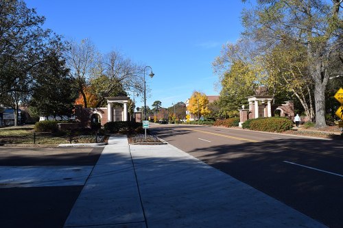 Entrance to a tree-lined street with decorative pillars and colorful autumn foliage under a clear blue sky.