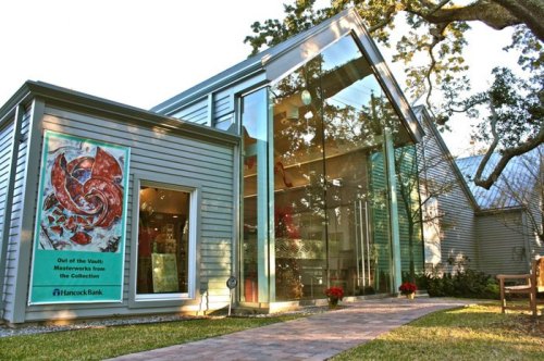 Modern bank building with large glass windows, surrounded by greenery and featuring a colorful art display outside.