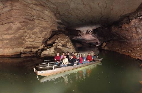A group of people on a boat in a dark cave, surrounded by rock formations and still water.