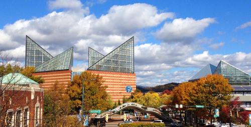 Modern buildings with triangular glass roofs surrounded by colorful autumn trees under a blue sky with clouds.