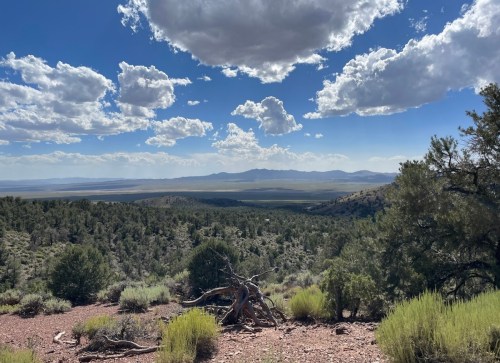 A panoramic view of a mountainous landscape with green vegetation and scattered clouds in a blue sky.