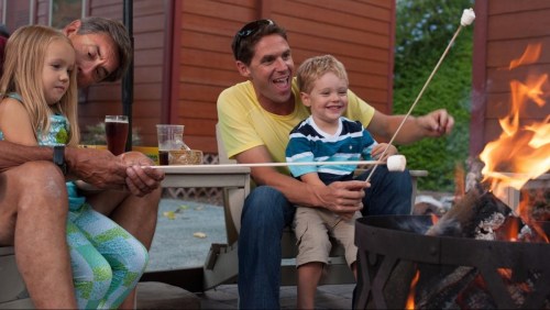 A family enjoys roasting marshmallows by a campfire, smiling and sharing a fun moment together outdoors.