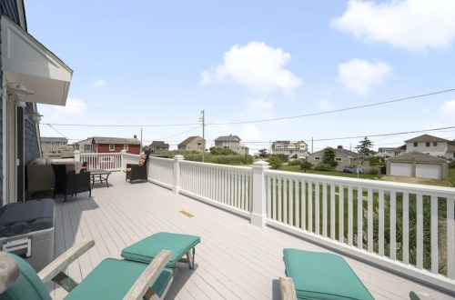 A spacious deck with lounge chairs overlooks a coastal neighborhood and blue sky.
