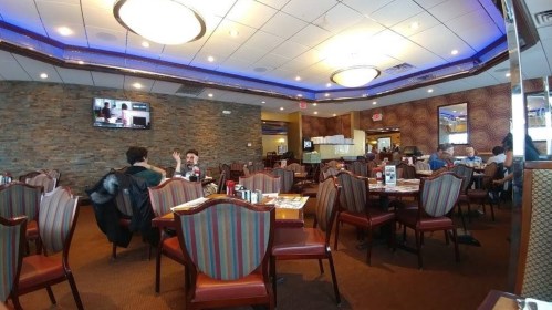 A spacious restaurant interior with striped chairs, tables set for dining, and a few patrons enjoying their meals.