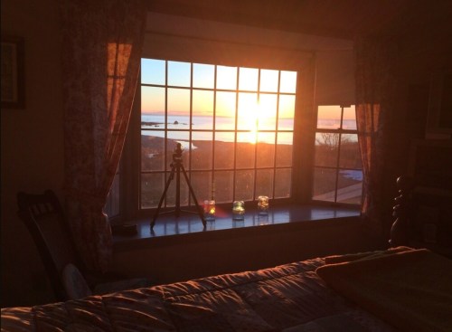 Sunset view from a window, with a camera on a tripod and colorful candles on the windowsill.