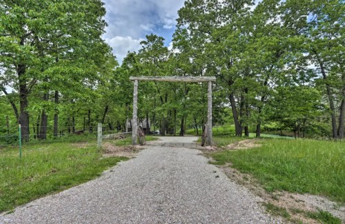 A gravel path leads through lush greenery to a wooden archway surrounded by trees under a partly cloudy sky.