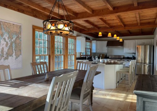 Bright kitchen and dining area with wooden beams, a large table, and modern appliances, featuring a map on the wall.