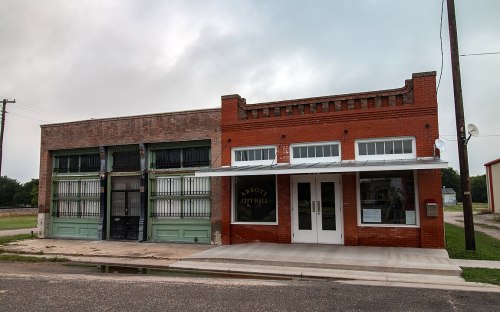 Historic city hall building with red brick facade, large windows, and a neighboring structure with green accents.
