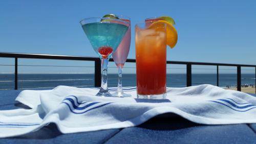 Three colorful cocktails on a table with a beach view, featuring a blue drink, a pink drink, and a vibrant orange drink.