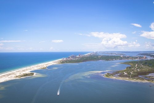 Aerial view of a coastal landscape with sandy beaches, blue waters, and a distant city skyline under a clear sky.