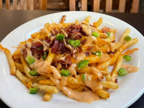 A plate of loaded fries topped with cheese, bacon, green onions, and a drizzle of sauce.