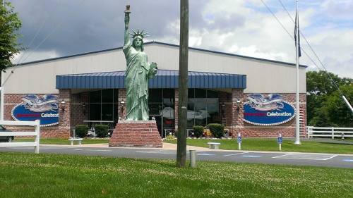A replica of the Statue of Liberty stands in front of a building with "American Celebration" signage.