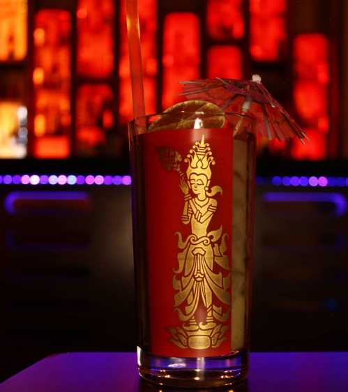 A colorful cocktail in a glass featuring a decorative design, with a straw and a small umbrella, set against a vibrant bar backdrop.